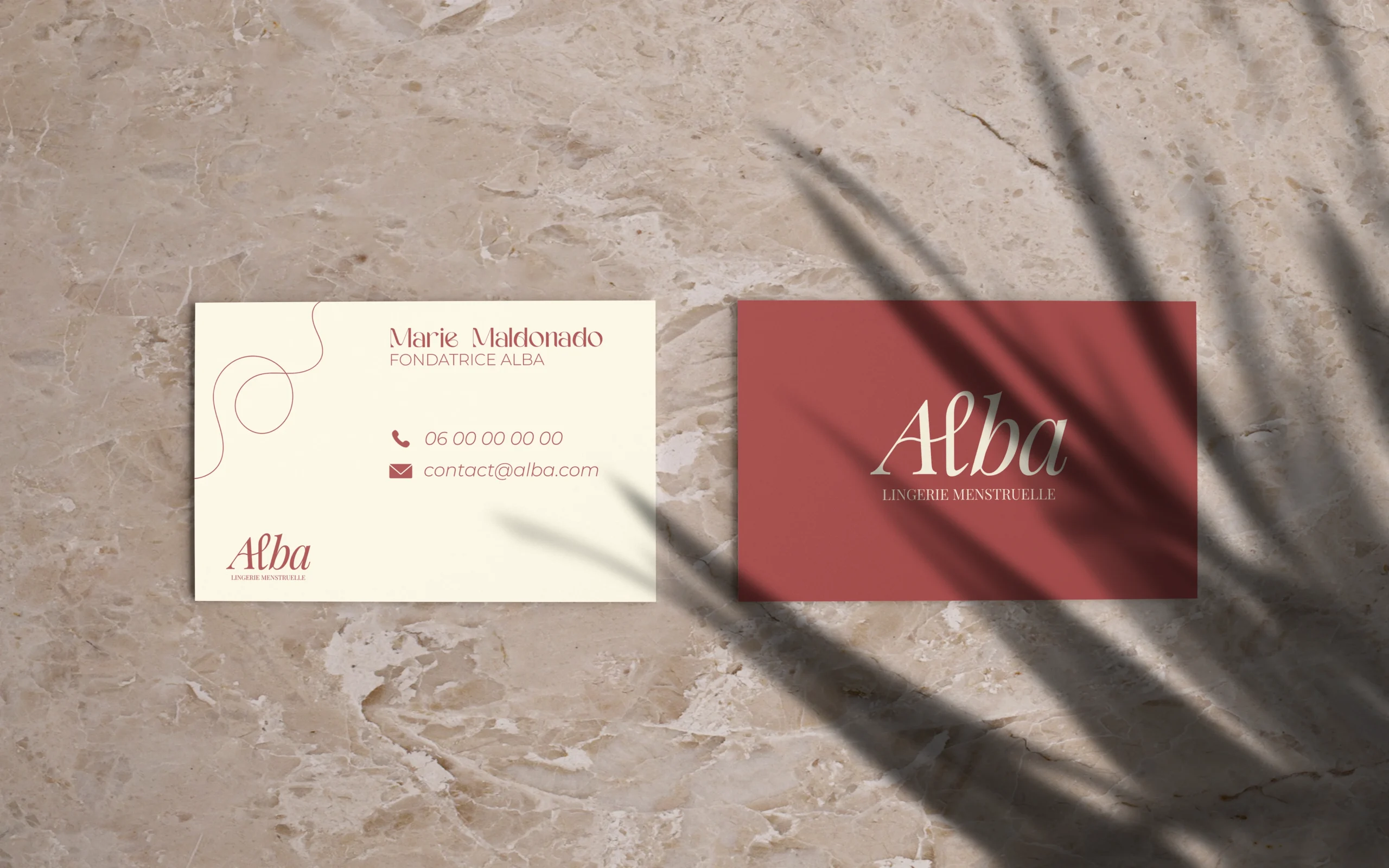 Cartes de visite de la marque Alba, lingerie menstruelle, posées sur une surface en marbre clair avec ombre de feuillage